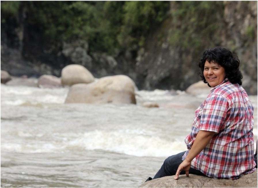 A photo of Berta Caceres sitting on a rock and looking over her shoulder to smile at the camera.