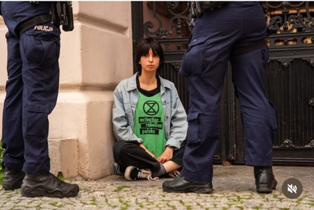 Buntowniczka siedząca na ziemi. Dwóch policjantówobok